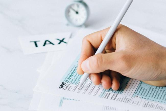 Decorative image of a hand holding a pencil, filling out tax forms